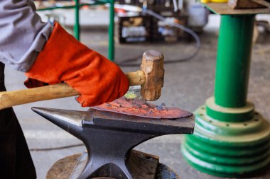 Zanaatkar, balta hazırlama atölyesinde çekiç kullanarak örsün üzerinde metal şekillendiriyor..