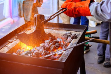 Demirci maşayla ısıtılmış metali şekillendirir, balta yaparken zanaatta yanan kömürlerle çevrilidir.