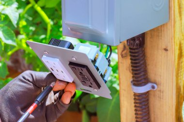 Elektrik işçisi bahçe ayarlarında elektrik erişimi sağlamak için USB portlarını, bir açık hava prizine bağlıyor.