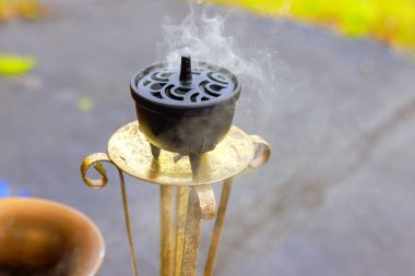 Tütsü, duman yükselirken dekoratif tütsü tutacağının üzerinde oturur. Açık havada sakin bir atmosfer yaratır.
