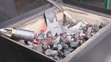 Demirci, metal işçiliğinin balta yapımı sırasında parlayan kömürlerin üzerinde büyük metal aletleri ısıtır..