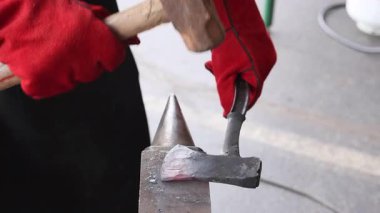 Yetenekli zanaatkar şekilleri koruyucu eldiven giyerken örsün üzerinde parlayan baltalar yapıyor..