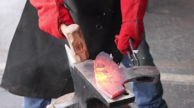 Zanaatkar, balta hazırlama atölyesinde çekiç kullanarak örsün üzerinde metal şekillendiriyor..