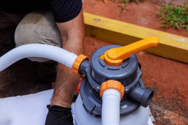 Servis çalışanı havuz filtresi üzerinde çalışıyor, arka bahçedeki temizlik işlerinde ideal performans için bağlantıları ayarlıyor.