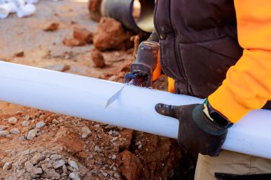 Yetenekli işçiler inşaat alanında malzemelerle çevrili plastik boruları kesmek için el testeresi kullanır..