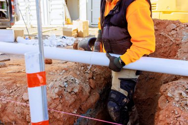 İnşaat işçisi PVC borusunu sipere yerleştirirken çevresi aletlerle çevrili..