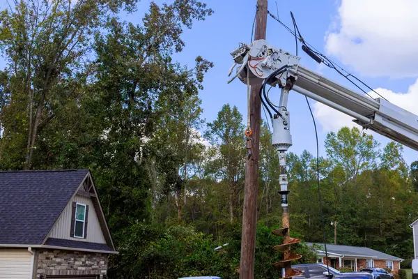 Elektrik işçileri, ağaçlarla çevrili güneşli mahallelerdeki evlerin yakınlarındaki elektrik hatlarını onarmak için çalı kullanıyorlar..