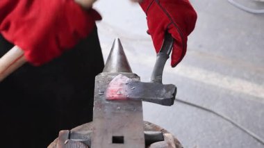 Bir zanaatkar koruyucu eldiven giyerken örsün üzerinde parlayan balta şekilleri yapar..