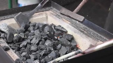 Zanaatkar, kızgın kömürlerle, aletlerle çevrili iken baltalamak için erimiş metali şekillendirerek demircide özenle çalışır.