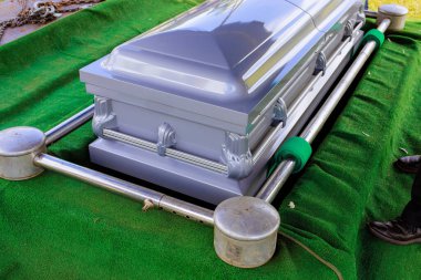 Gri metal tabut, cenaze hazırlıkları sırasında mezarlığın kasvetli atmosferinde dinleniyor.