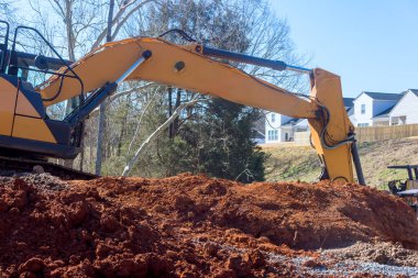 Ağır makineler inşaat sahasında kazı yapıyor çünkü evler iş alanına bakıyor
