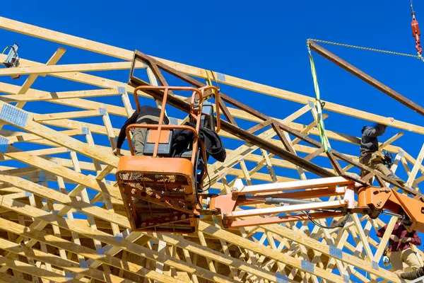 İnşaat işçileri, temiz mavi gökyüzünün altında ahşap çatı kirişlerini monte etmek için asansör kullanıyorlar..