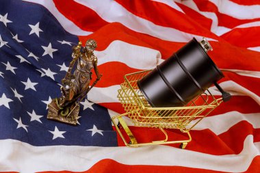 İçinde siyah yağ varilleri olan alışveriş arabası canlı Amerikan bayrağıyla birlikte Adalet Anıtı 'nın küçük heykelinin yanında.
