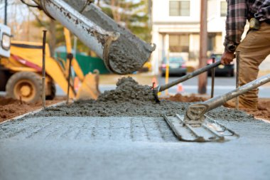 Çalışan işçiler, inşaat faaliyetlerinin ortasında kaldırım için yeni beton dökerler.