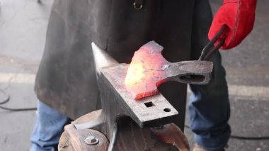 Zanaatkar, balta yapımında parlayan metali şekillendirmek için çekiç kullanır..