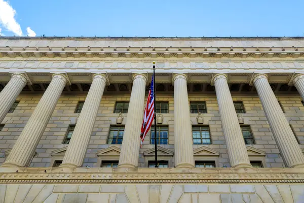 Uzun sütunlar, açık mavi gökyüzü altında Amerikan bayrağını gösteren hükümet binasını destekliyor..