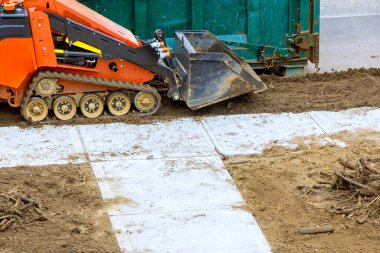 Ağır makineler, büyük çöp konteynırının yanındaki kaldırım tesisatı için hassas bir zemin hazırlıyor..
