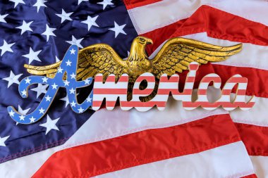 Vurucu altın kartal, Amerikan bayrağını sallayarak ulusal gururu sembolize eden Amerika sözcüğünün üzerinde yatıyor..