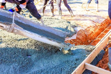 İnşaat işçileri çalışma günlerinde inşaat alanındaki temel zemine taze beton döküyorlar.