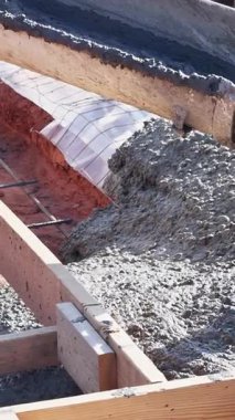 İnşaat işçileri, yerleşim alanındaki yeni temel kaplaması için ahşap formlara taze beton döküyorlar.