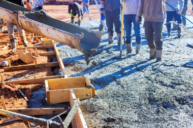İşçiler inşaat alanındaki inşaat günlerinde ahşap formlara taze beton döküyorlar.