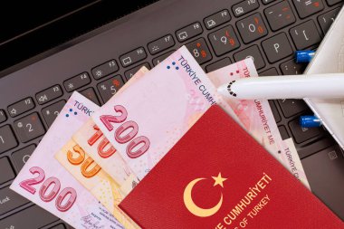 Para birimi lira banknotları ve Türkiye pasaportu dizüstü bilgisayar klavyesinde bulunuyor, seyahat planlama finansal durumunun göstergesi.