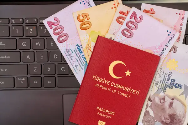 Türk pasaportu seyahat hazırlıkları sırasında çeşitli lira banknotlarıyla birlikte dizüstü bilgisayarın klavyesinde yer alıyor.