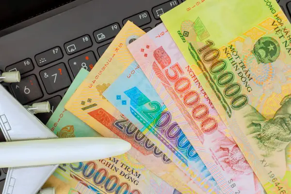 Vietnam dong nakit para birimi küçük uçak modelinin yanında dizüstü bilgisayarda dinleniyor, seyahat planlarını ima ediyor.