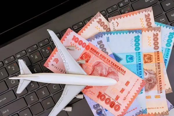 Seyahat hazırlıkları sırasında etrafında Tanzanya şilini bulunan dizüstü bilgisayar klavyesine yerleştirilmiş bir uçak..