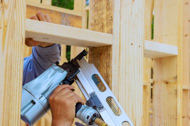 İşçi inşaat alanında pnömatik çivi tabancası kullanarak ahşap yapı oluşturuyor.