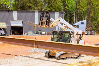 Tekerlek dümen yükleyicisi dikkatle kaldırır, iş günü inşaat alanında çelik kirişler yerleştirir.