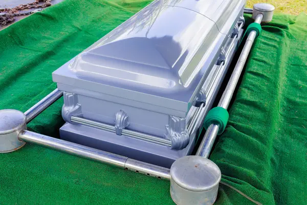 Cenaze için hazırlanmış tabut aydınlık gün ışığında sakin bir mezarlıkta canlı yeşil bir çimenlikte duruyor..