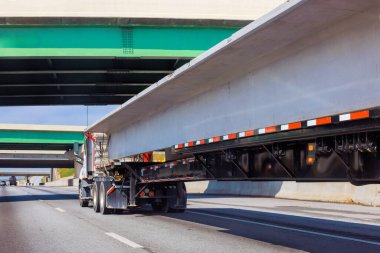 Kamyon, açık bir günde üst geçitlerle çevrili uzun beton levhalar taşıyor..