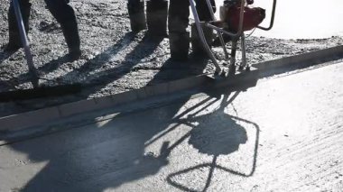 Çalışan işçiler, inşaat faaliyetlerinin ortasında kaldırım için yeni beton dökerler.
