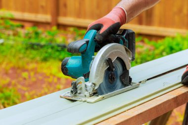 İşçiler iş saatinde arka bahçede PVC kaplama tahtalarını dairesel testereyle kesiyorlar.