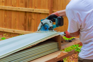 Sanatçı arka bahçede çalışırken ön cephe kaplamasını kesmek için elektrikli testere kullanıyor.