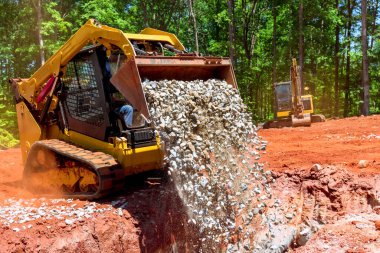 Buldozer kayaları sipere yerleştirirken başka bir makine de arazi temizliği sırasında peyzaj alanı hazırlıyor.