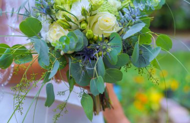 Beyaz güllerle, yeşilliklerle, gelinin bahçede tuttuğu mor aksanlarla dolu gelin buketi..