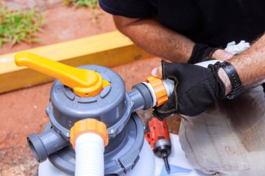 Skilled technician fixes pool filter pump system components while working in backyard