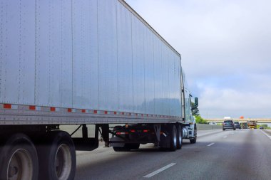 Büyük kamyon Amerikan otoyolu boyunca sürekli hareket ediyor. Arka plandaki diğer araçlar ise bulutlu gökyüzünün altında..