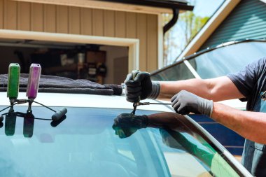 Teknisyen özenle araba ön camları üzerinde çalışır garajda eski eşyaları çıkartır, hassas değişimler için araçlar kullanır.