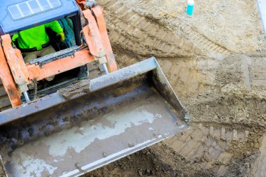 İnşaat işçisi gündüz vakti makineleri çalıştırırken kazıcı toprağı eşeliyor.