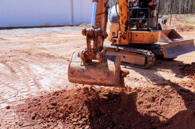İnşaat işçisi inşaat alanındaki zemini yeniden şekillendirmek için bir kazıcı çalıştırıyor.