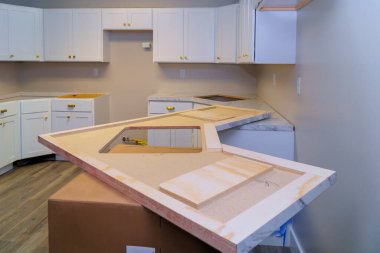 İnşaat işçileri çağdaş mutfağa beyaz dolaplı mermer tezgah kurmaya hazırlanıyorlar..