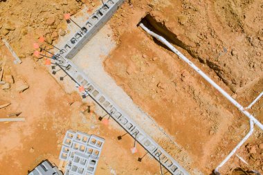 İşçiler, temel çalışma alanındaki inşaat sahasındaki tesisat tesisatı için siper kazıyorlar.