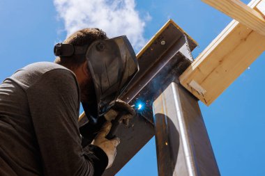 Müteahhit inşaat sahasında çelik kirişleri birleştiriyor, ve kıvılcımlar uçuşurken dikkatle göreve odaklanıyor.