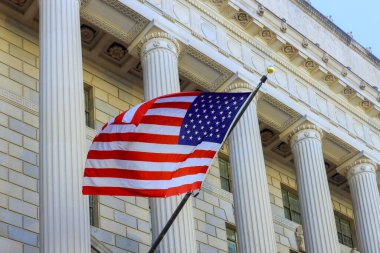 Büyük hükümet binasının önünde heybetli mimari sütunlarla dalgalanan bir Amerikan bayrağı..