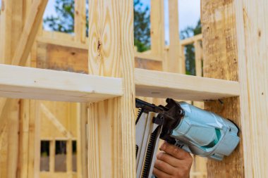 İşçi, yeni ev inşaatı projesinde tahta kirişleri güvence altına almak için hava çivi tabancası kullanıyor.