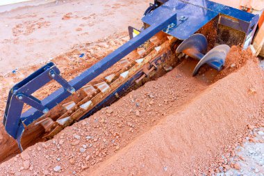 Ağır siper ekipmanları aktif bir inşaat bölgesinde yeraltı tesislerine hazırlanırken toprağı öğütüyor.