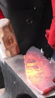 Zanaatkar, balta hazırlama atölyesinde çekiç kullanarak örsün üzerinde metal şekillendiriyor..